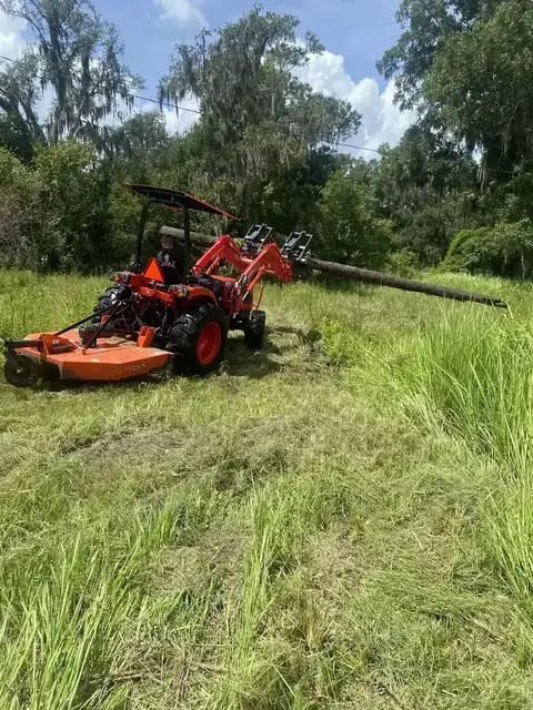 Kubota tractor using a grapple attachment to move brush and debris during property cleanup