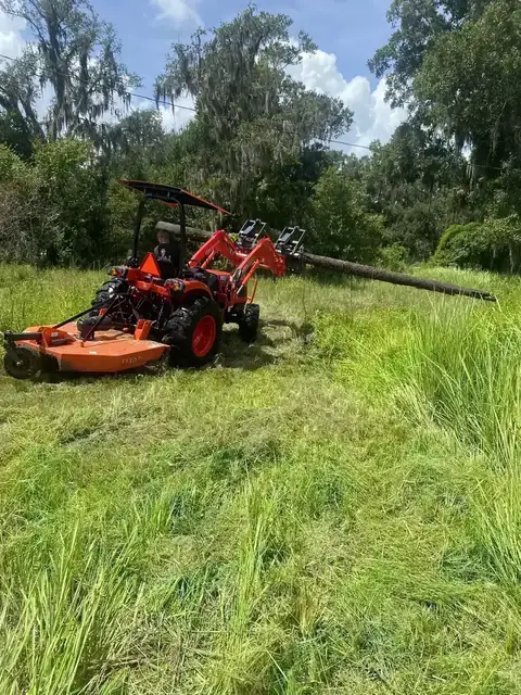 Kubota tractor using a grapple attachment to move brush and debris during property cleanup